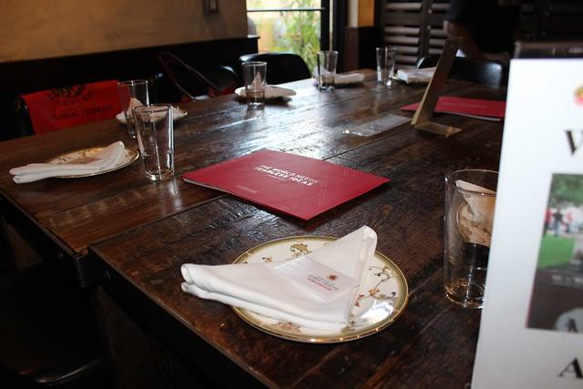 A wooden table is neatly set with glasses, ornate plates, and napkins.