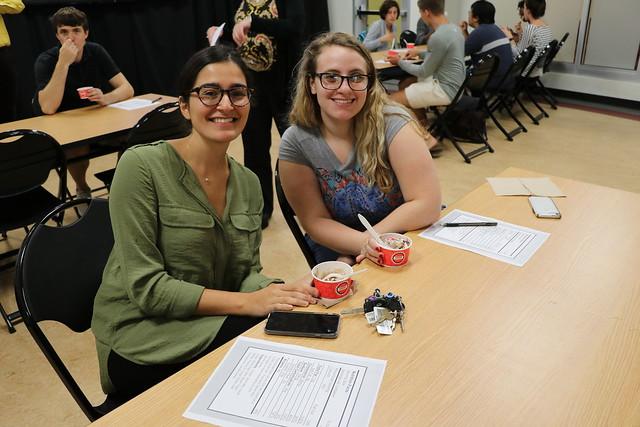 Two people smiling and eating ice cream at a conference table.