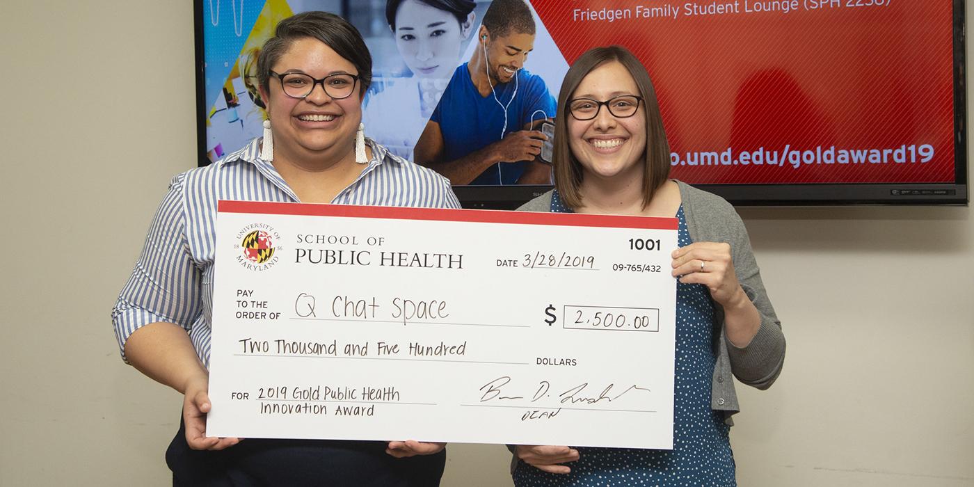 Tasha Williams and Jessica Fish holding large, fake check for $2,500 to represent winning the Gold Award