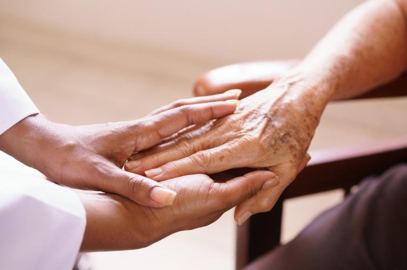 Old people in geriatric hospice: Aged patient receives the visit of a female black doctor. They shake their hands and talk in the hospital.