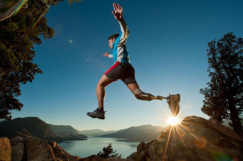 Man who has prosthetic leg jumping off a rock 