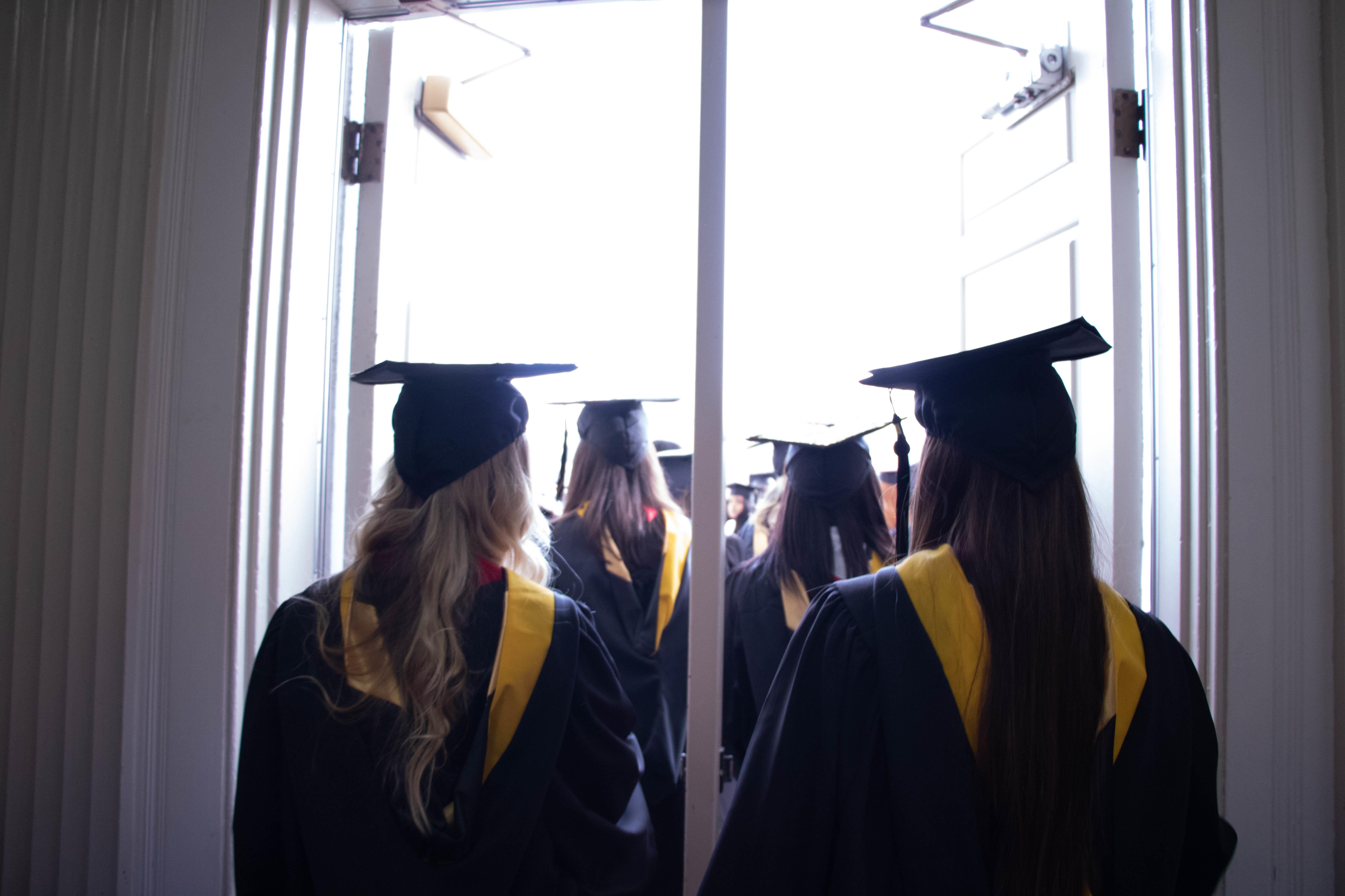 Students wearing caps and gowns walking out of a building 