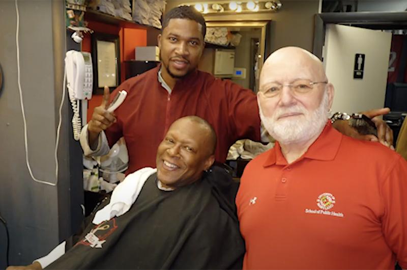 Three men at the barbershop, smiling at the camera. Two are African American, one White.