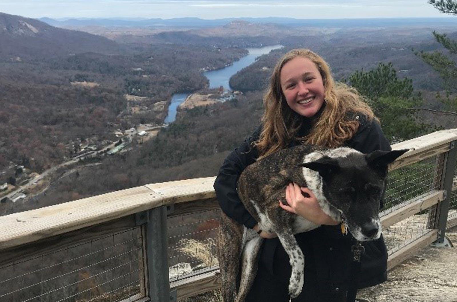 Student from the University of Maryland holding a dog standing by a fence overlooking a river valley