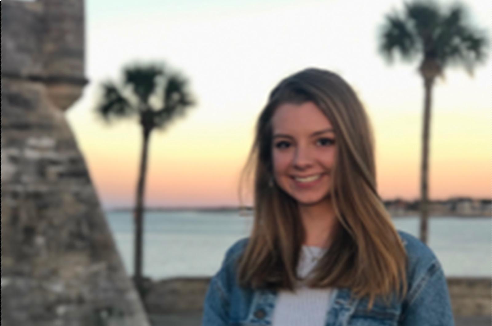 Student from the University of Maryland smiles at camera. Standing on a beach