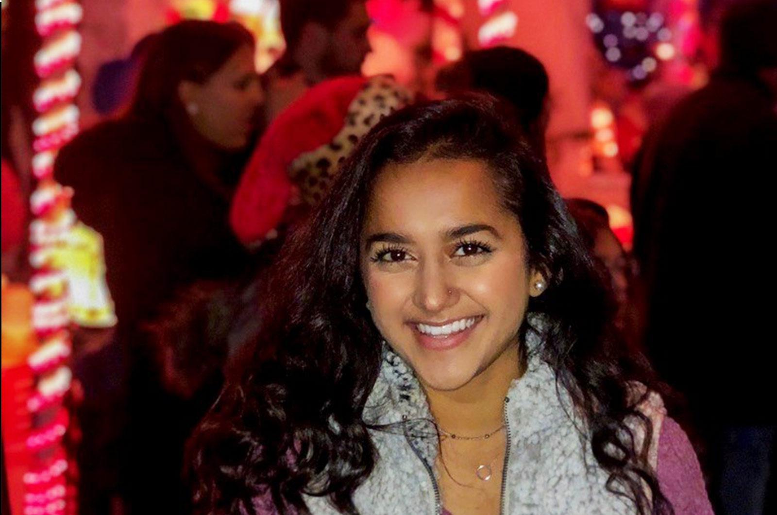 Student smiles at camera. Background is a holiday festival.