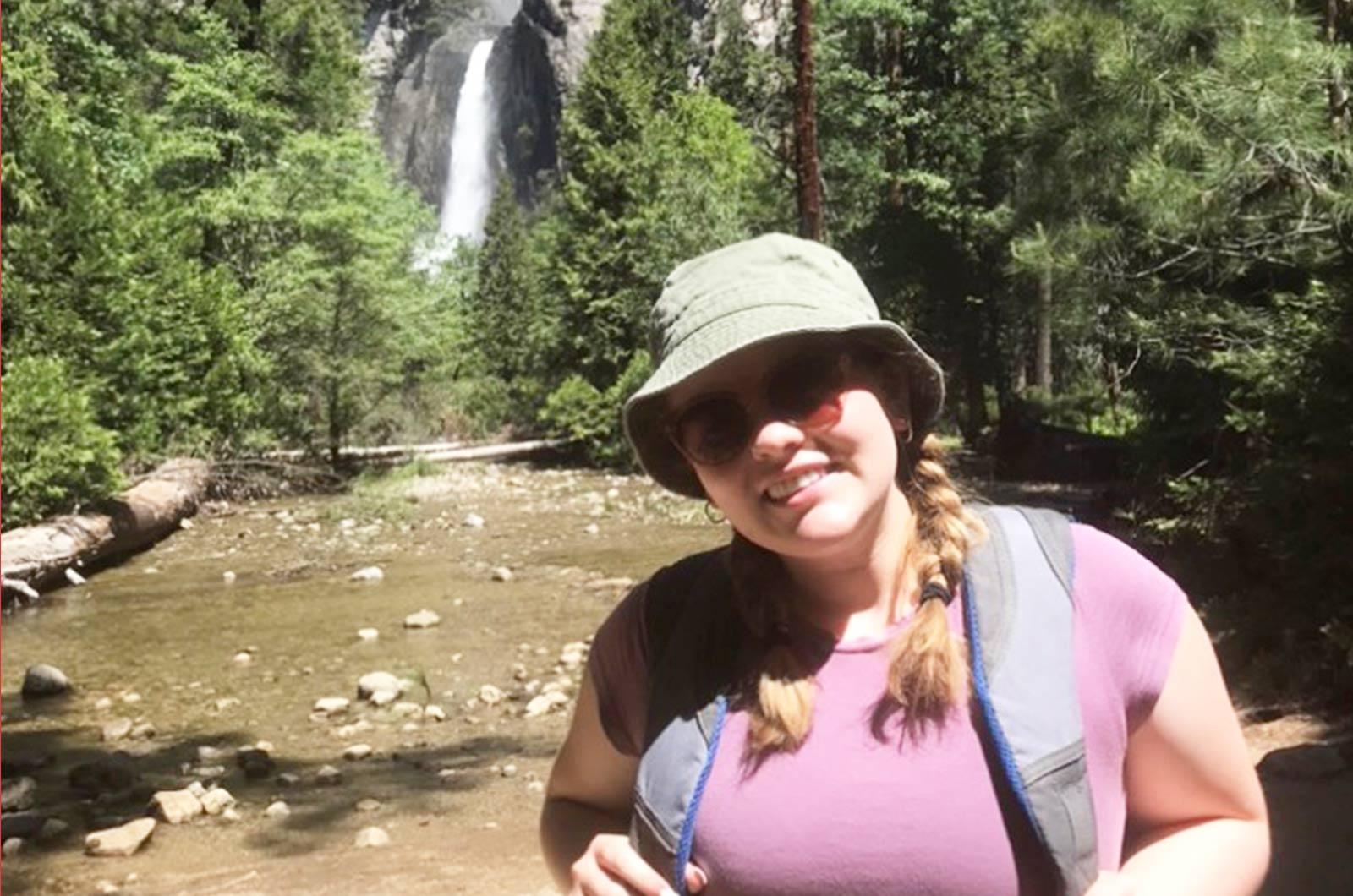 Student from the University of Maryland wearing sunglasses and hat poses in front of waterfall