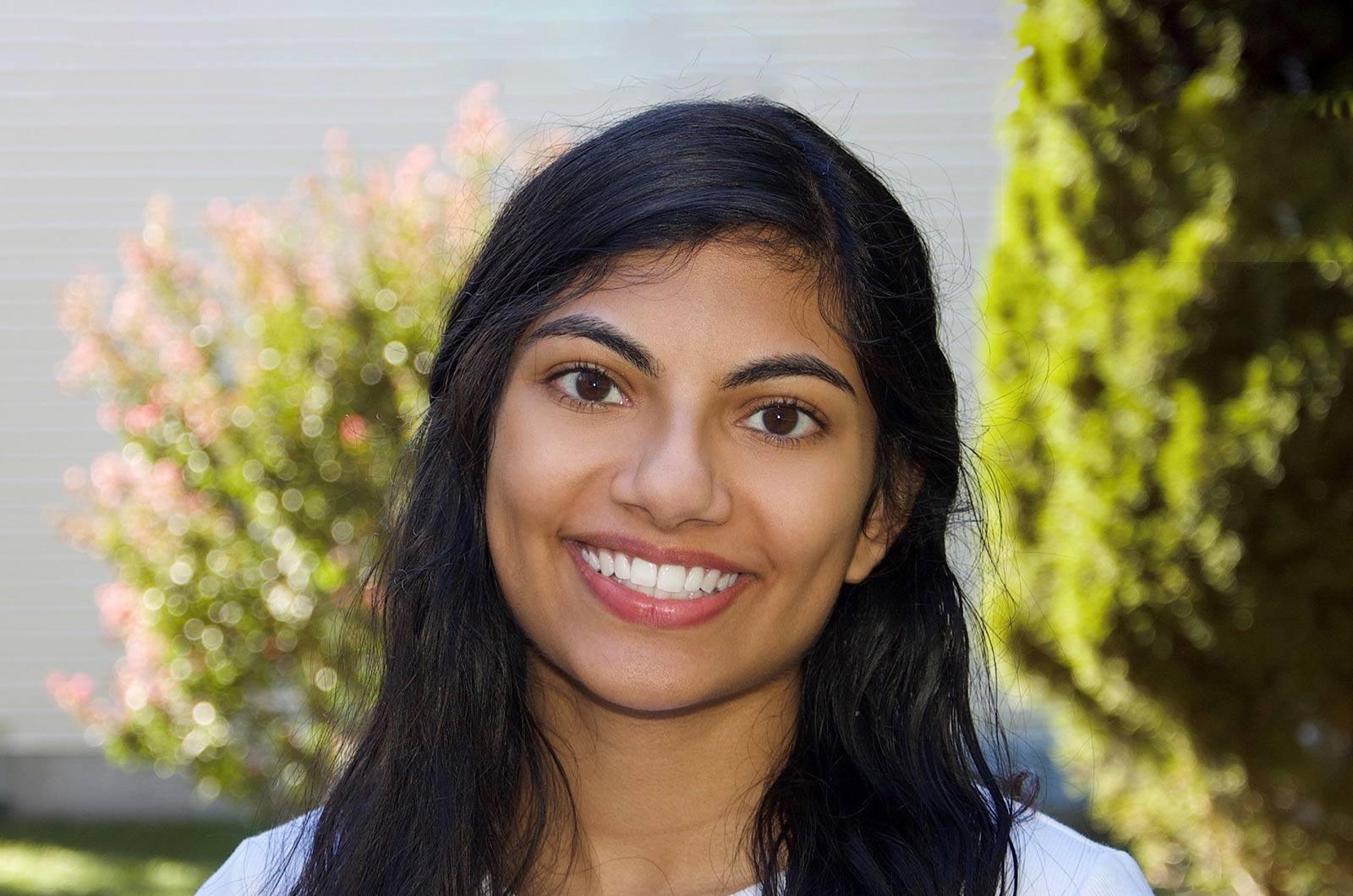 Student from the University of Maryland smiles at camera in front of flowering shrub