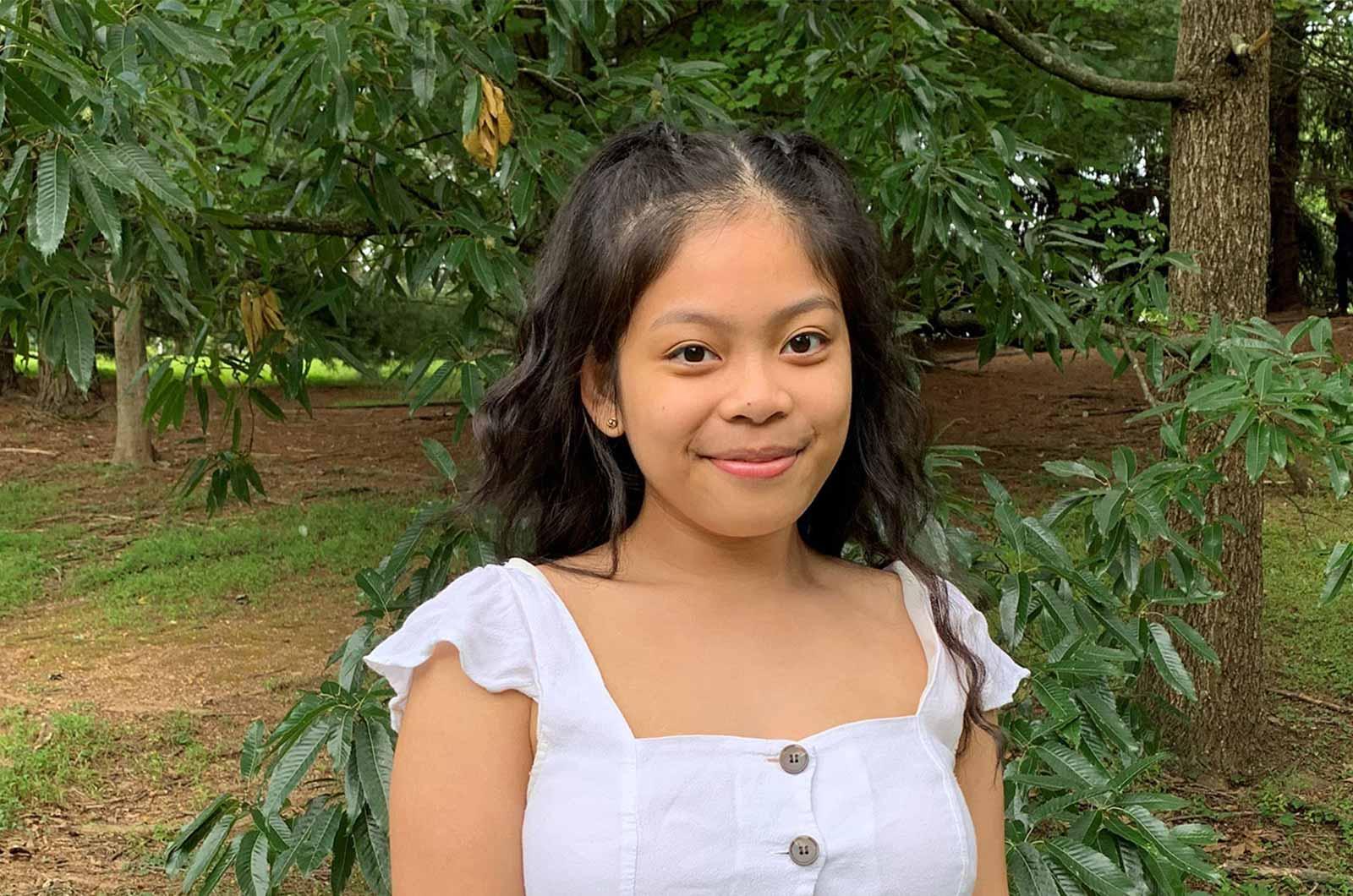 Student from the University of Maryland smiles at camera with trees in background