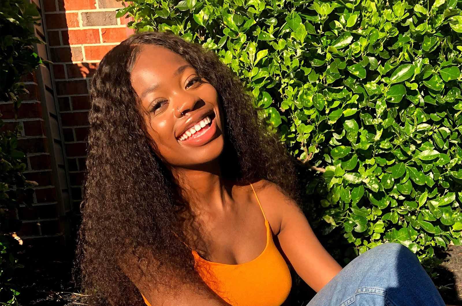 Student from the University of Maryland sitting in front of shrub and brick wall smiles at camera