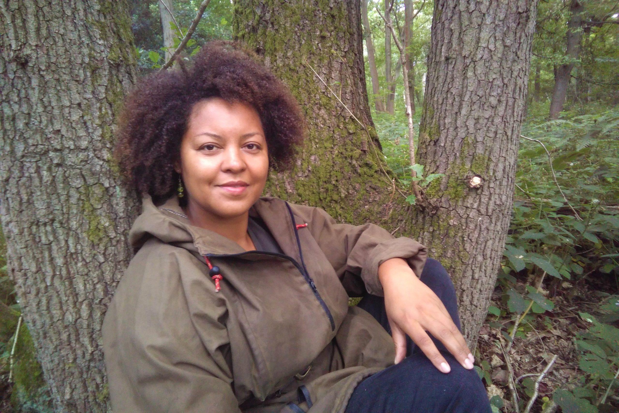 Beth Collier sitting on the ground, leaning on trees in the woods