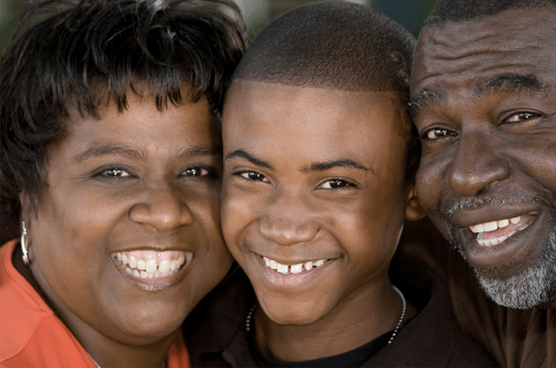 Close up photo of Black woman, boy and man smiling with their heads close together