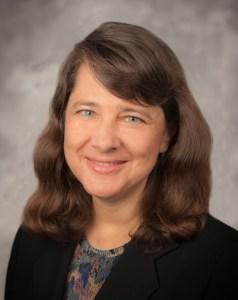 Cindy Brach with dark brown hair and wearing a black coat and patterned blouse.