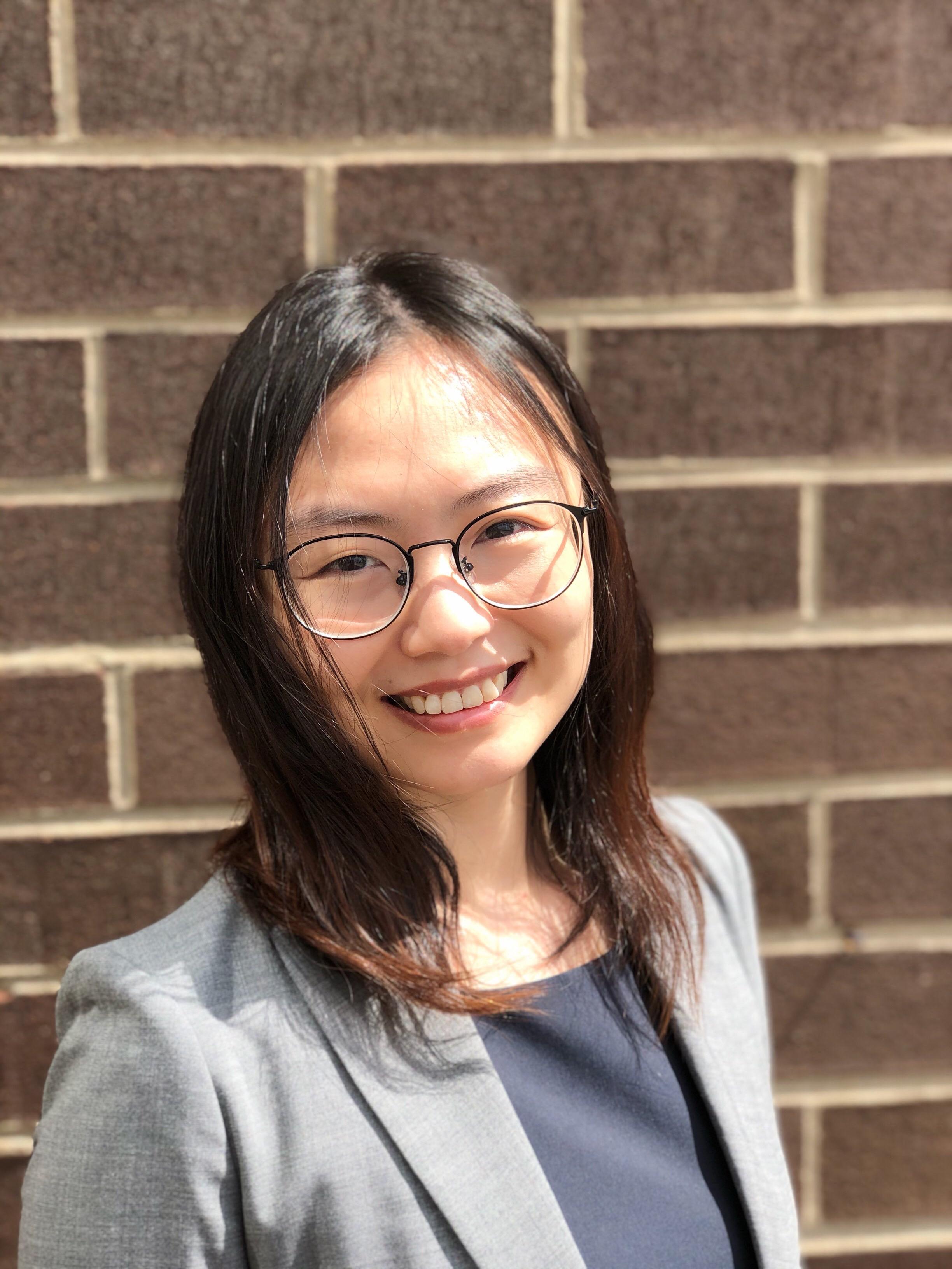 Liyang Xie with dark brown hair, wearing glasses, grey blazer and black garment