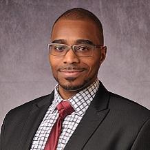 Rashawn Ray wearing glasses, red tie, white patterned shirt and black coat.
