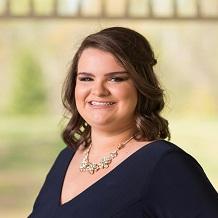 Taylor Palmer with brown hair wearing a necklace and dark blue garment.