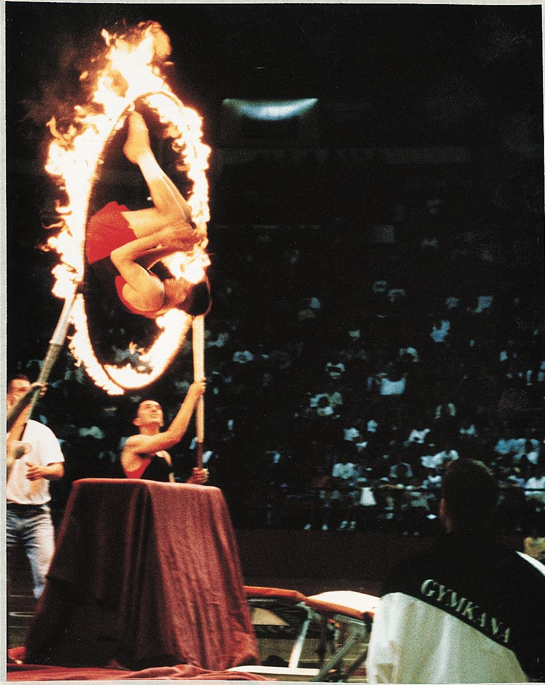 Member of Gymkana troupe flips through ring of fire that two others are holding up