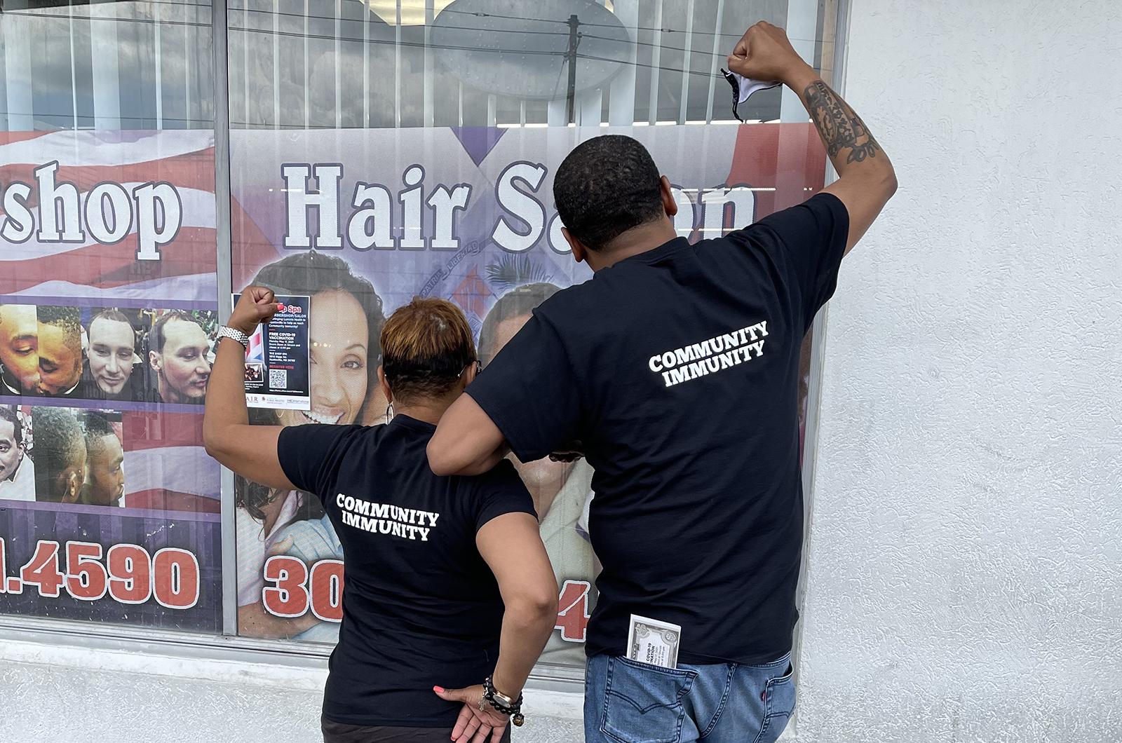 Katrina and Mike holding up their fists triumphantly and showing the back of their t-shirts which say "community immunity"