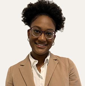 Kayla Foster wearing glasses, hoop earrings, white blouse and light brown blazer.