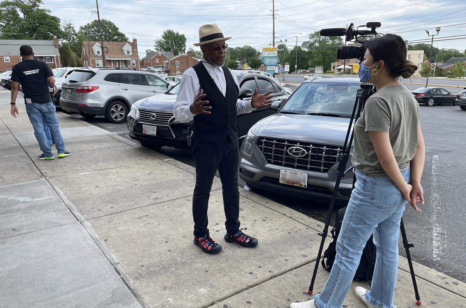 Stephen Thomas talks to a Washington Post reporter with a video camera on the sidewalk outside a barbershop.
