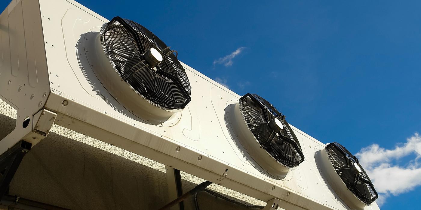 Photo of three large fans on the outside of a building with bright blue sky above
