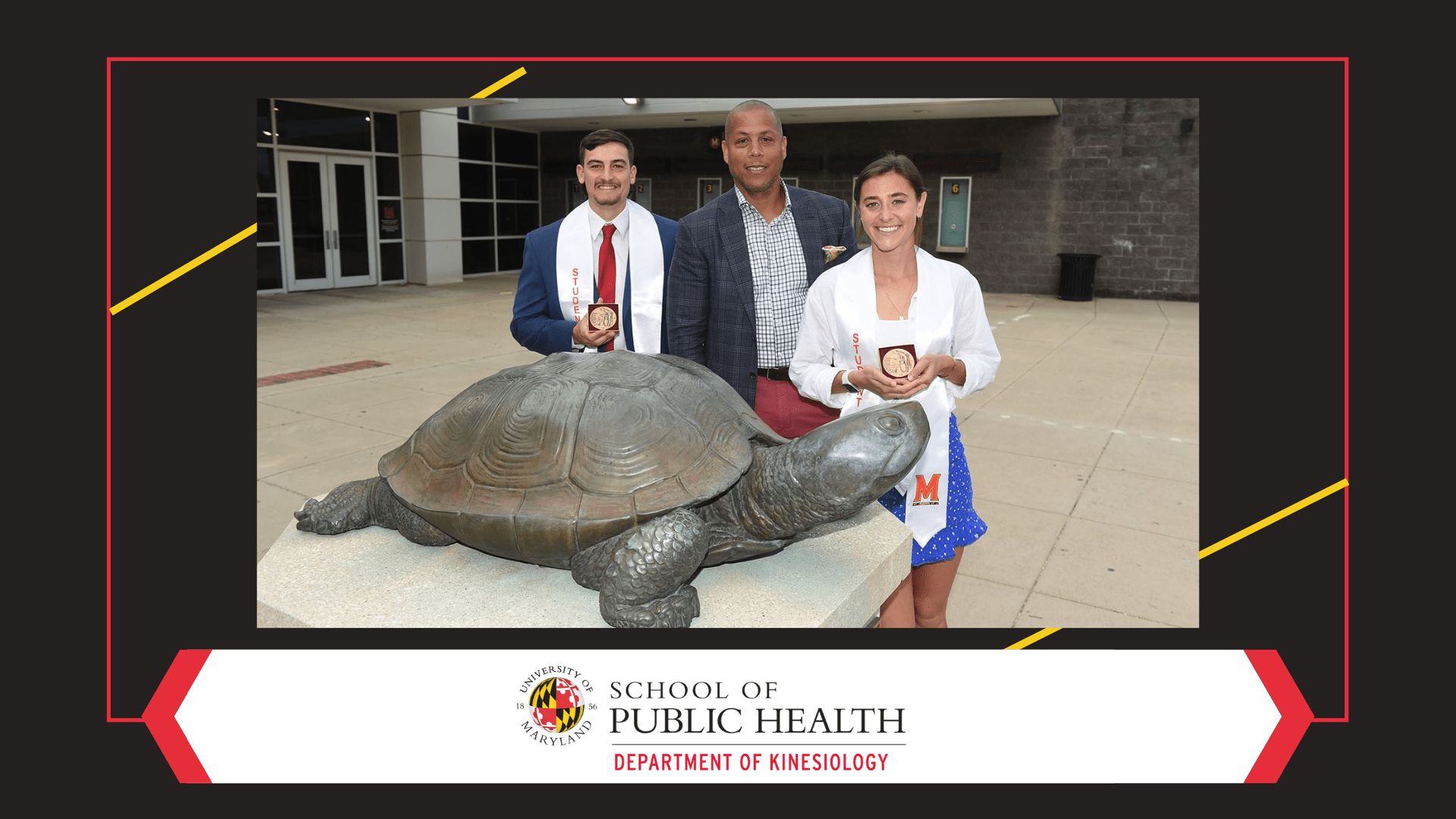 Two students stand holding trophies by Testudo statue