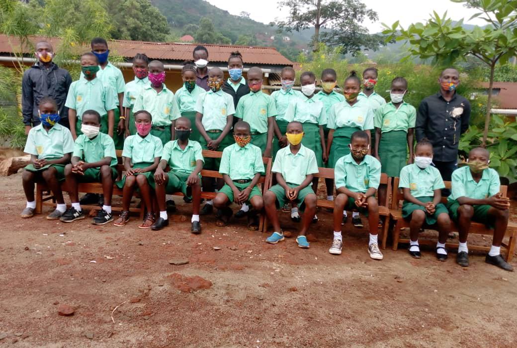 Two rows of children dressed in green school uniforms and wearing COVID-19 face coverings at the Abigail D. Butscher Primary School in Sierra Leone (Photo credit, M. Tholley.)