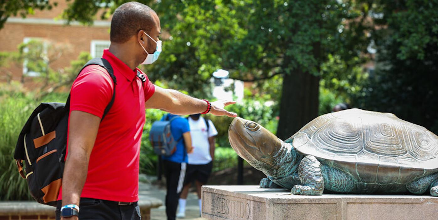 A student wearing a mask touching a UMD campus Testudo statue on the nose during COVID-19.