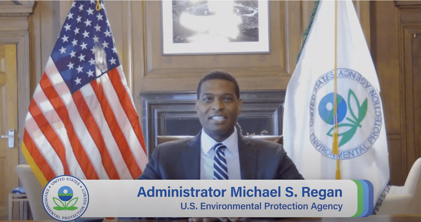 US EPA Administrator Michael S. Regan sitting at a desk with an American flag and EPA flag behind him.