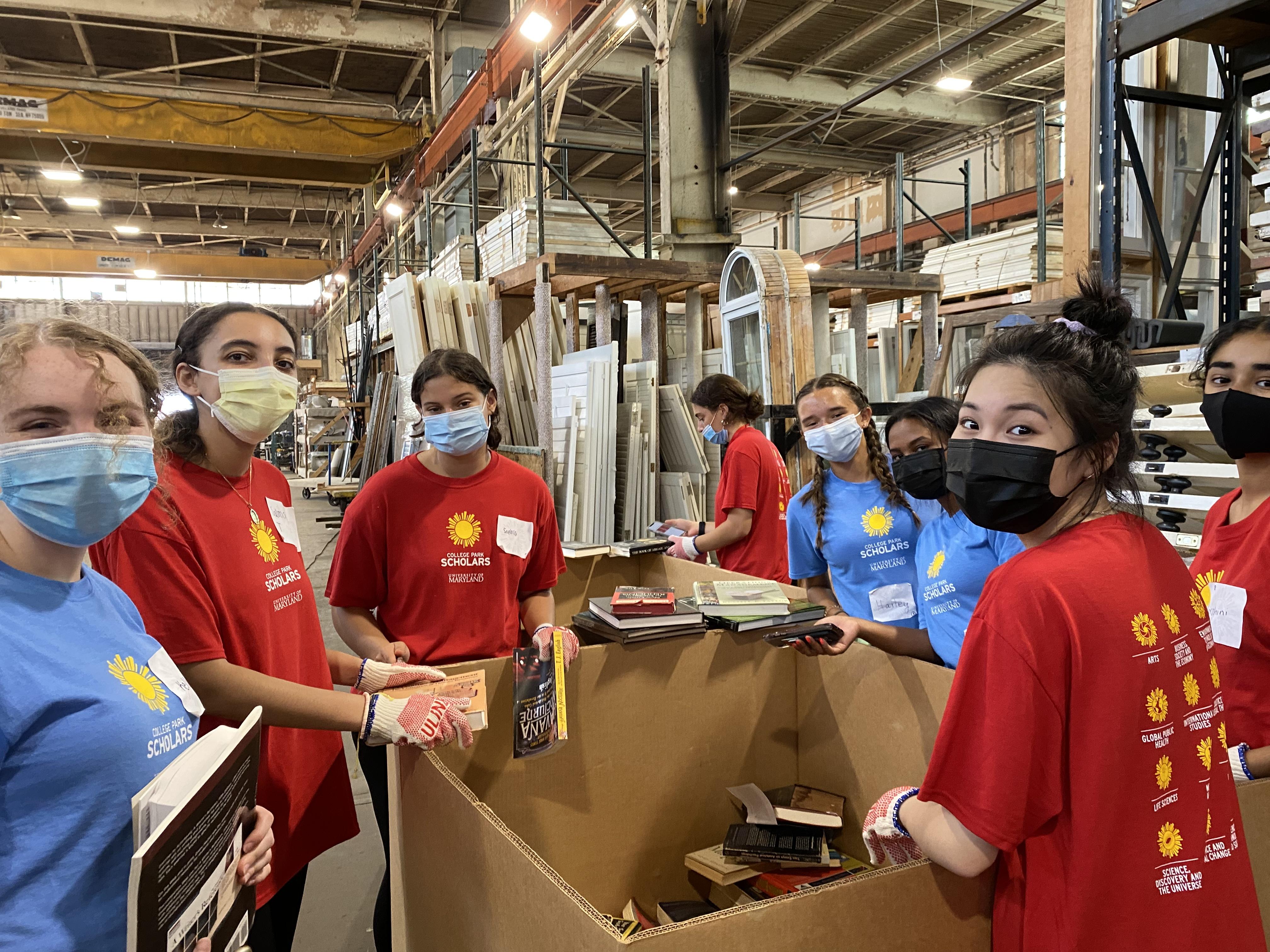 Seven global health scholars are standing around a large box in a Second Chance warehouse. They are wearing masks and looking at the camera.