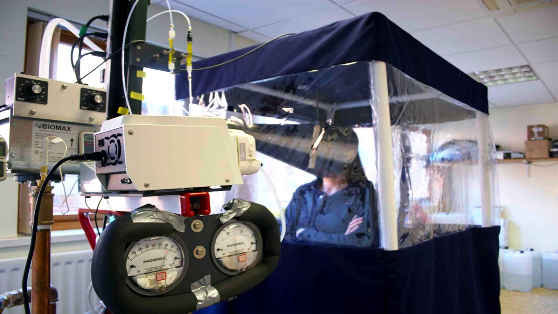 A person sits inside a booth called the Gesundheit II, which is used to collect their exhaled breath and test for virus transmission.