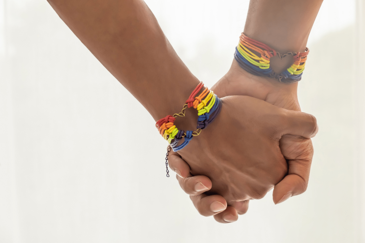 pair of black men holding hands and wearing gay pride rainbow bracelets.