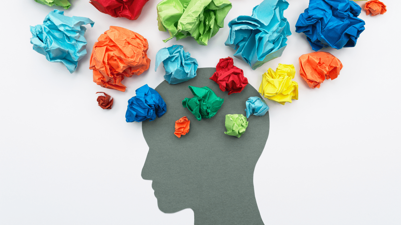 Silhouette of head with crumpled up colorful paper surrounding it like a cloud of thoughts