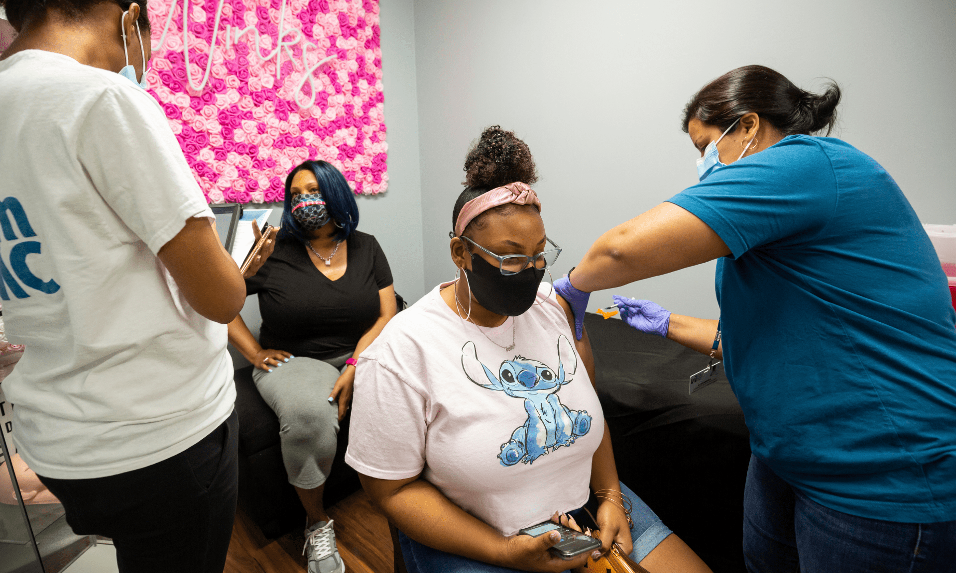 A young Black woman receives a COVID vaccine at a Black beauty salon with other women sitting nearby