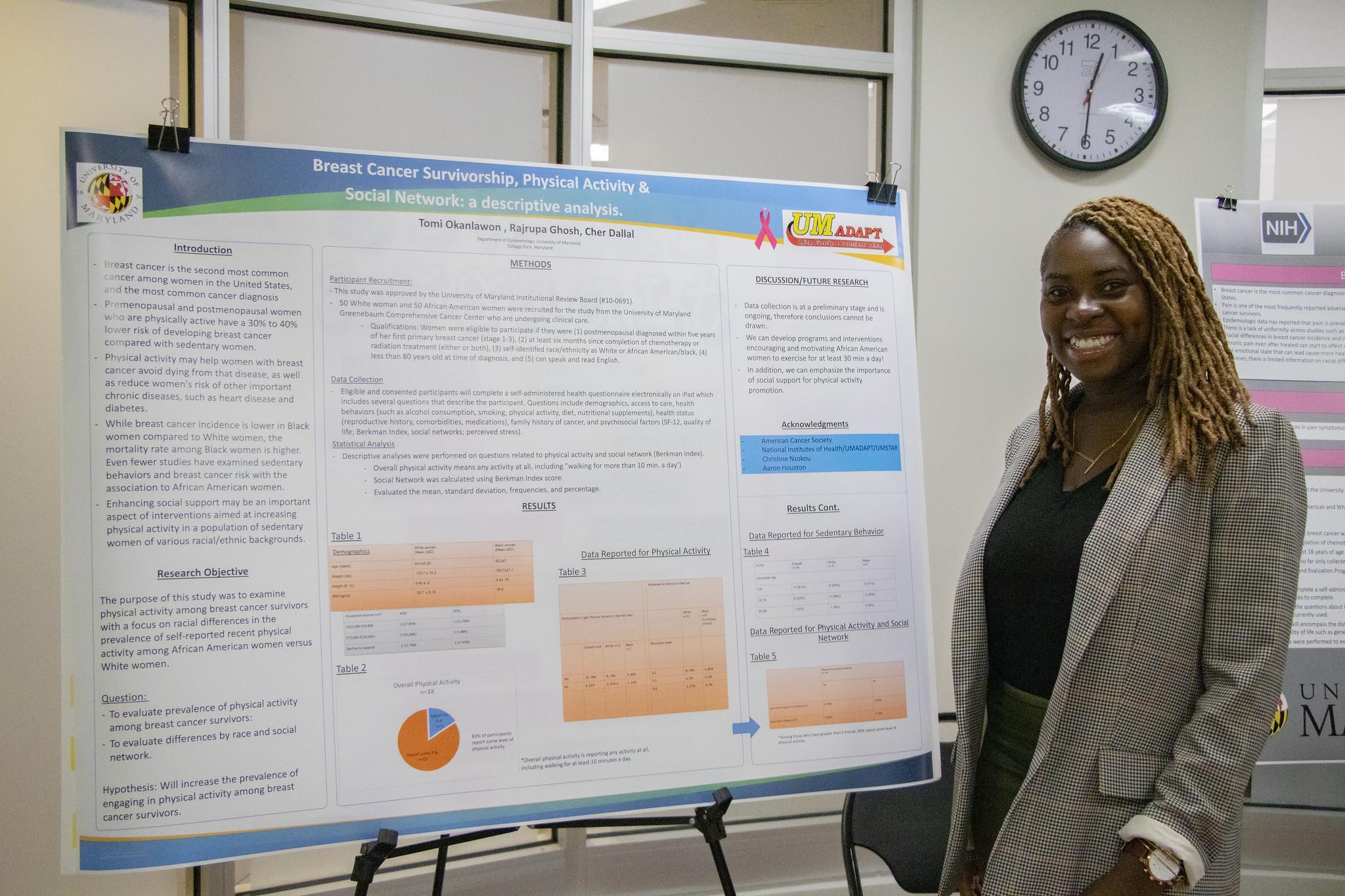 African American female student with braids and a suit jacket stands next to her research poster