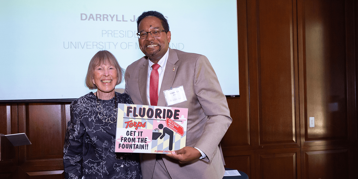 Dr. Alice Horowitz and President Pines smile holding a sign that says "Fluoride: Terps get it from the tap."