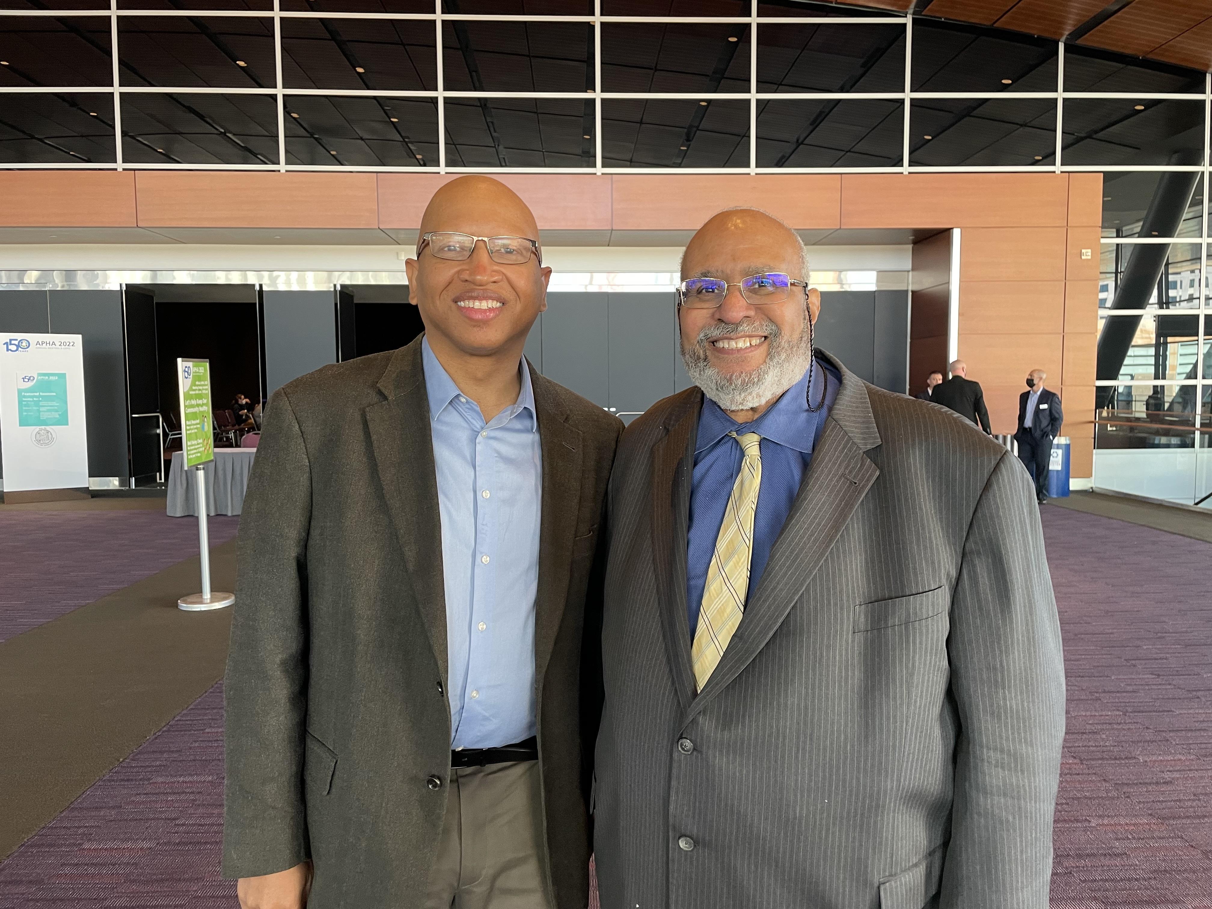 Sacoby Wilson, wearing a blue shirt and grey suit jacket, stands to the left of Dr. Georges Benjamin, executive director of APHA, who is wearing a blue shirt, yellow tie and grey suit jacket.