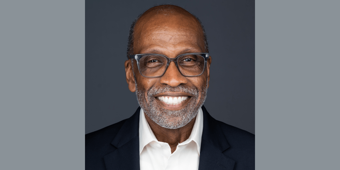 Man wearing glasses, black blazer and white shirt, smiling at the camera.