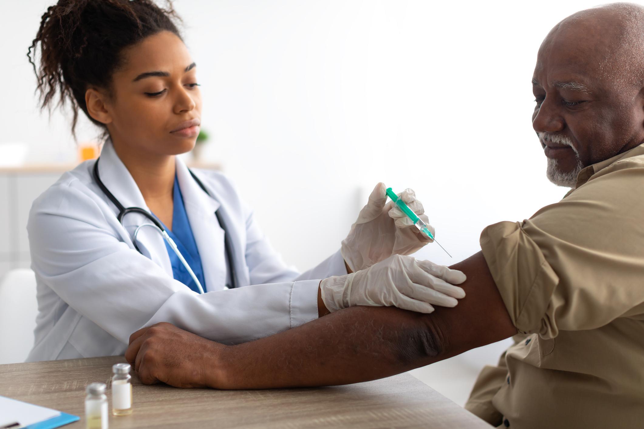 Black female doctor giving a black male senior citizen a covid vaccine shot