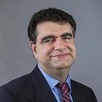 Man wearing black blazer, blue shirt and maroon and silver striped tie smiles at the camera.