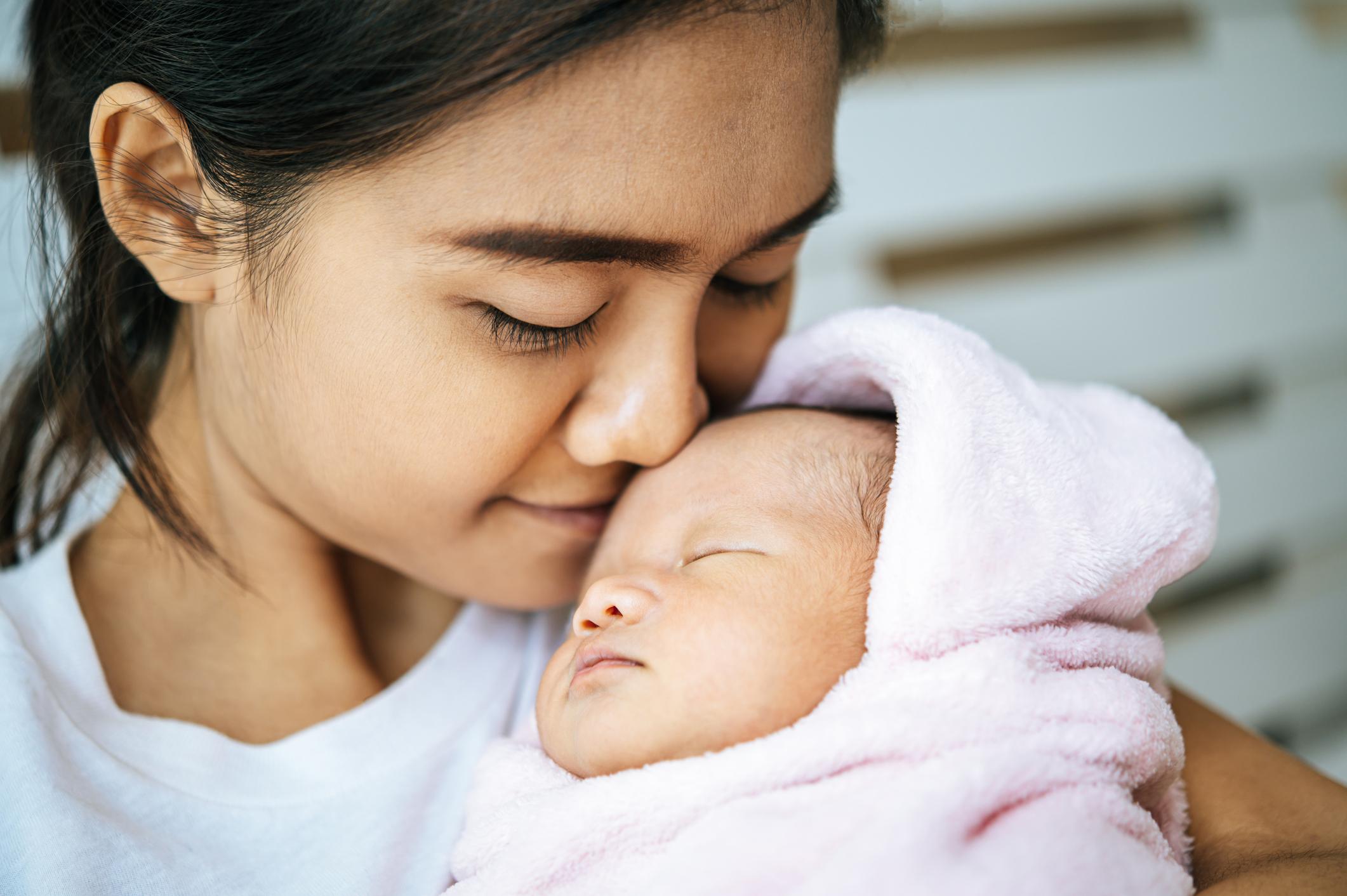 Woman cuddling her new born baby that is wrapped in a blanket