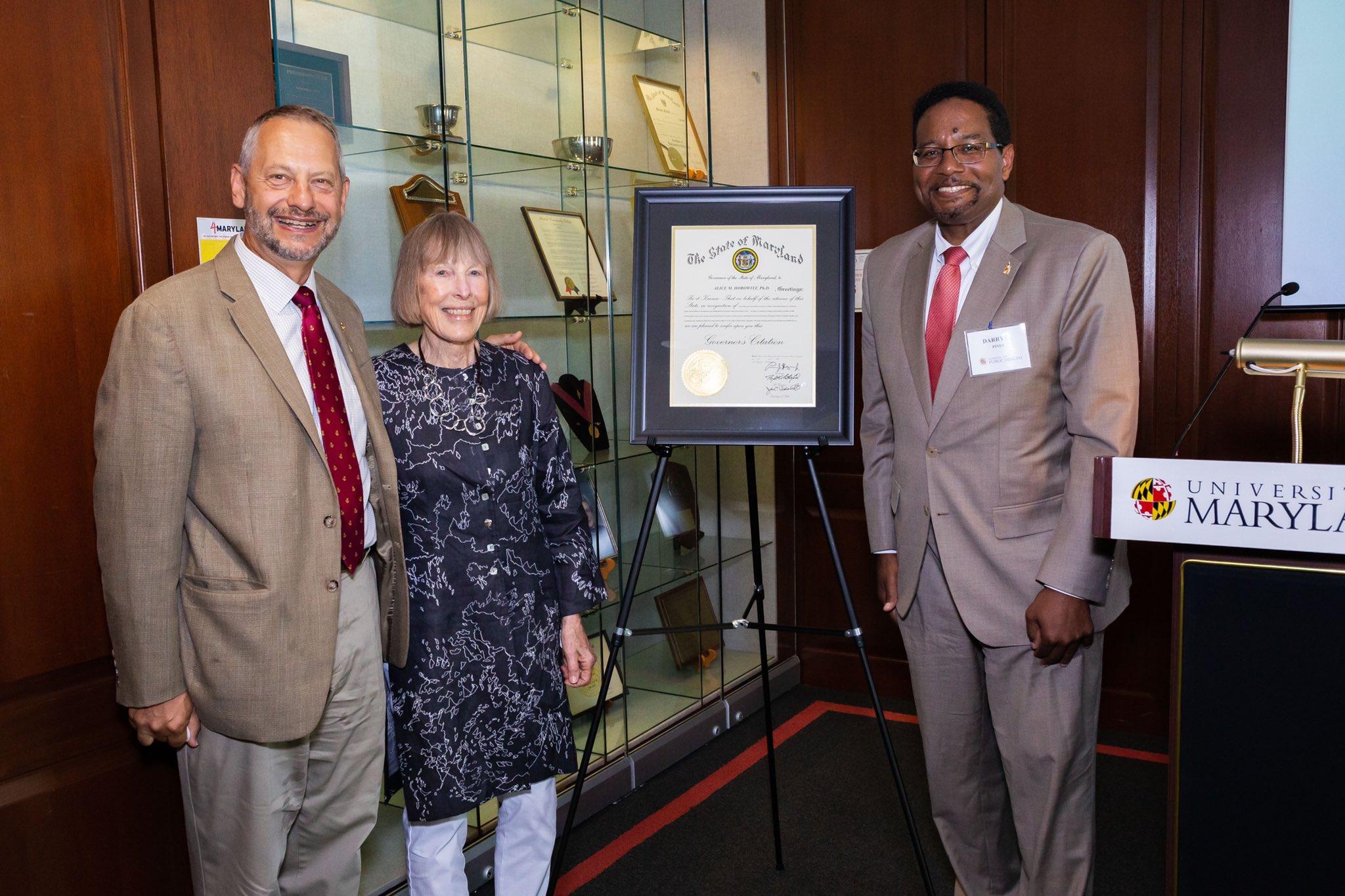 Two men and one woman, who is in the middle, stand near a Maryland state proclamation and a sign with the University of Maryland name on it.