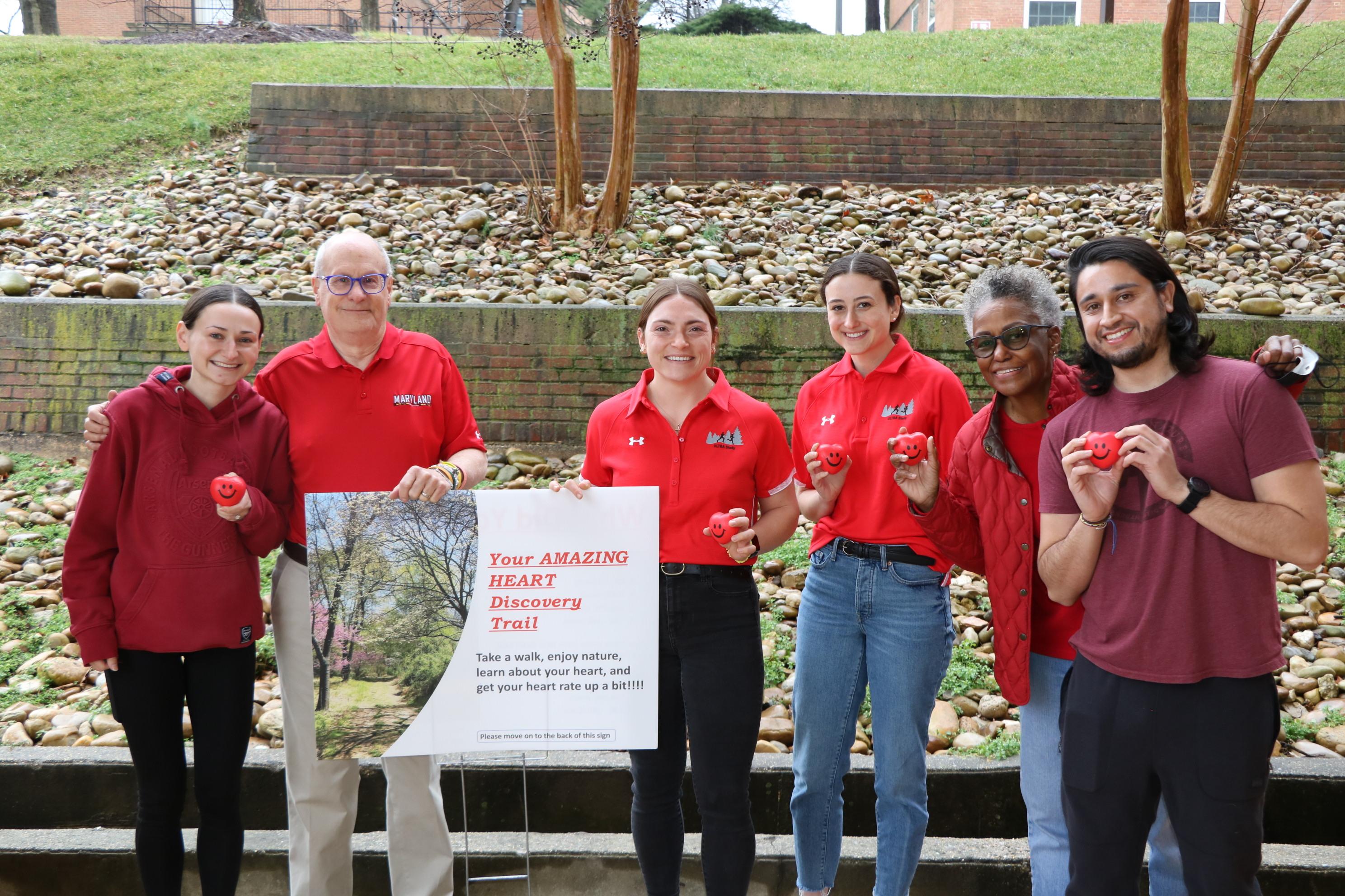 A group of men and women wearing red shirts and holding small, squeezable red foam hearts in their hands.