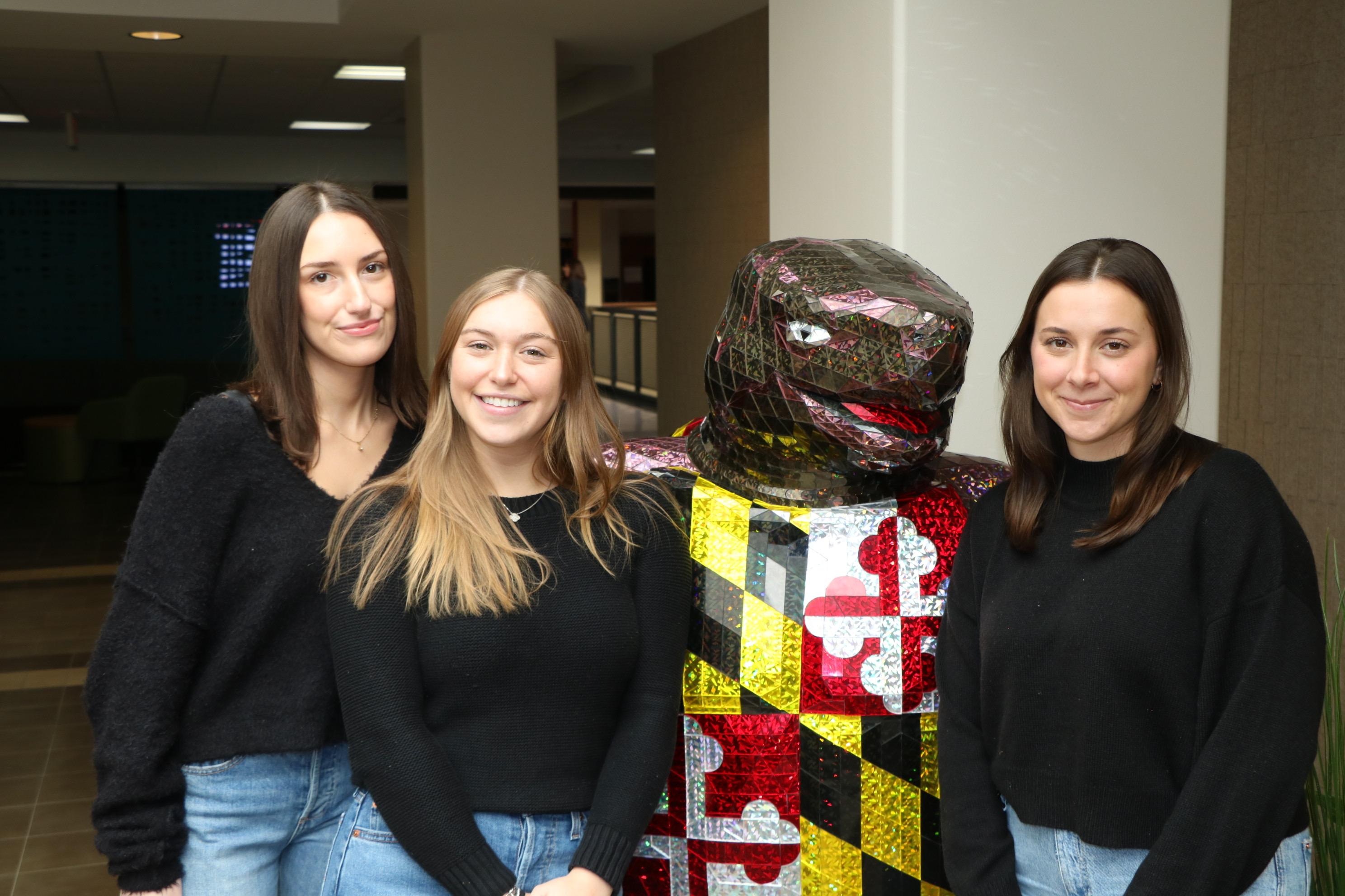 Three women posing for a photo with the UMD mascot.