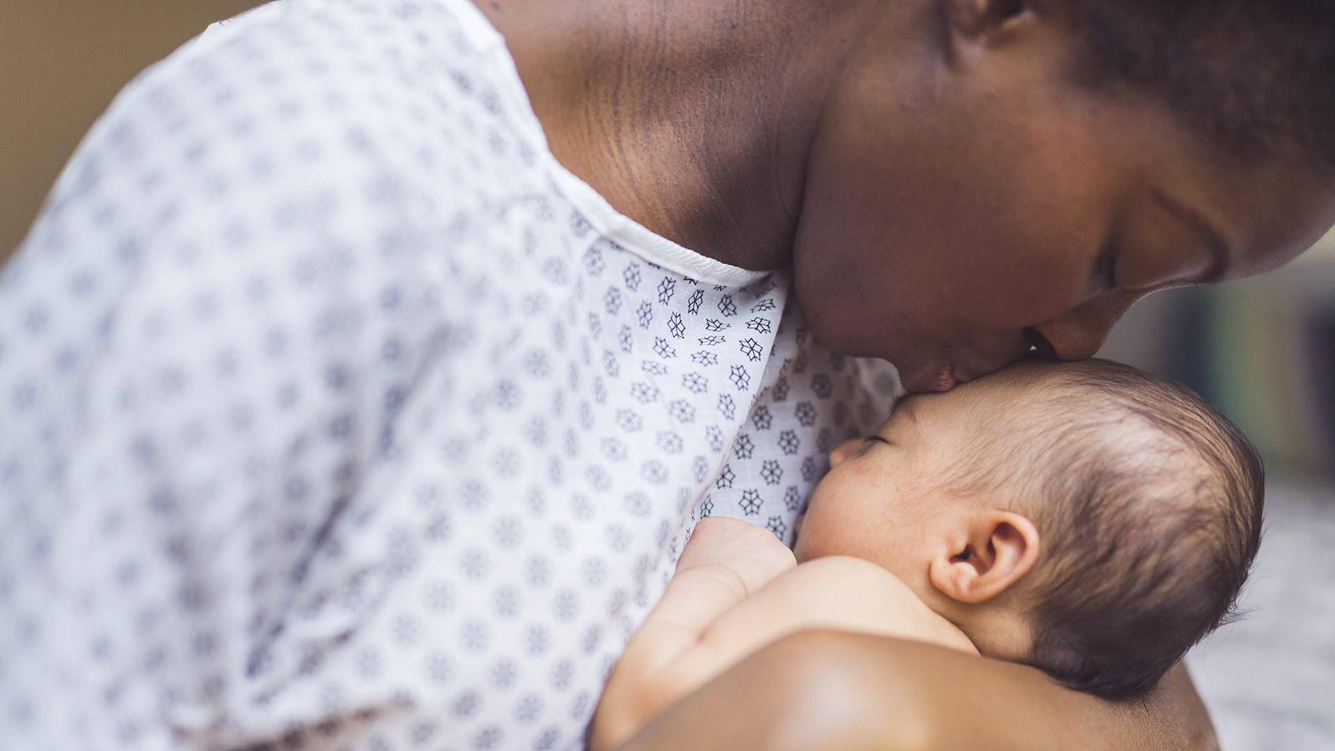 Woman wearing hospital gown embraces a newborn baby.