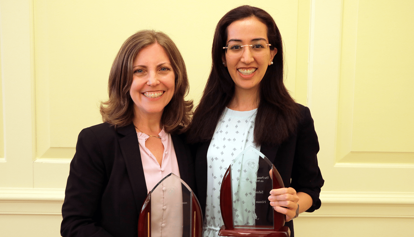 Professor Amy Sapkota and Sahra Ibrahimi stand next to each other holding glass-like awards.