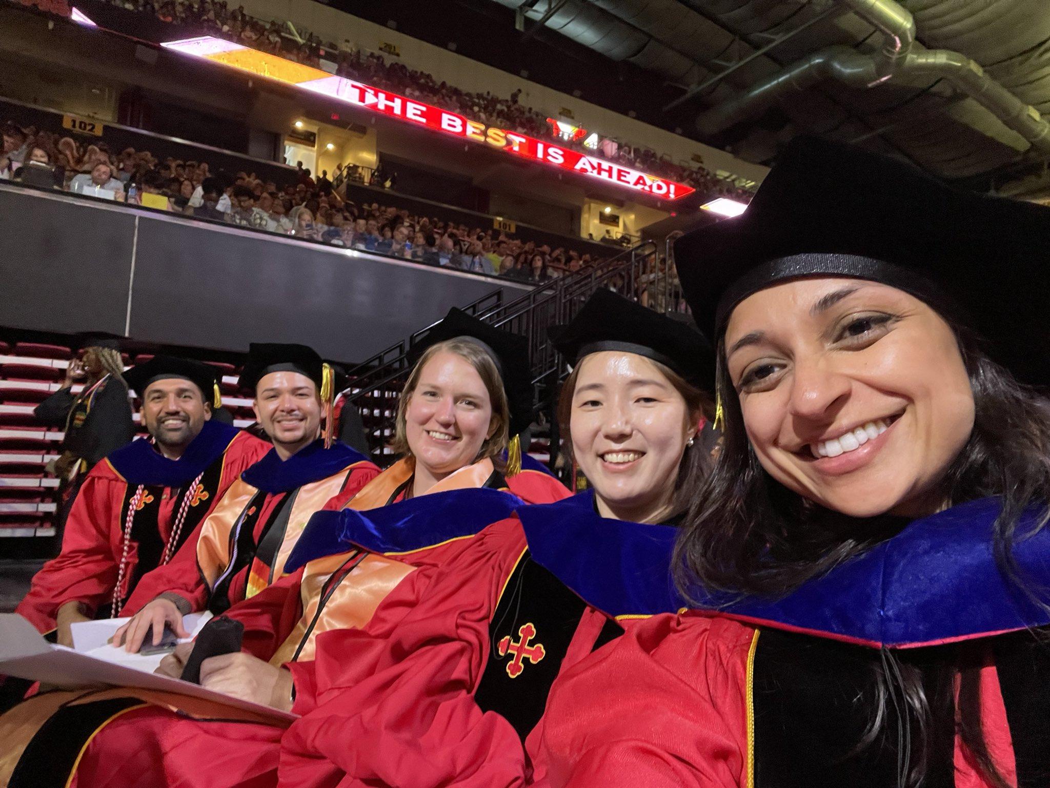 University graduates wearing red gowns and black caps during a commencement ceremony.