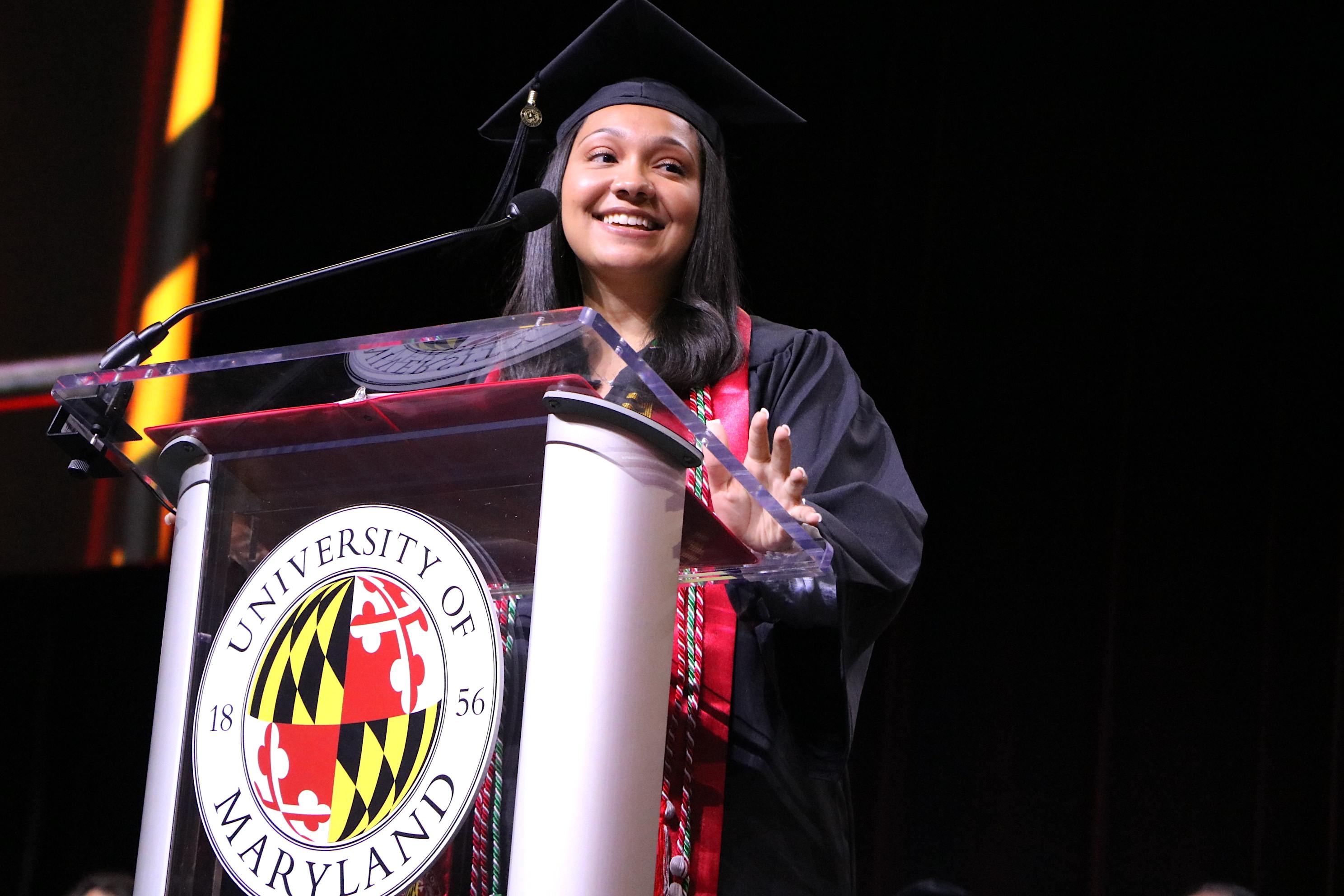 Female student wearing cap and gown speaks at a graduation ceremony.