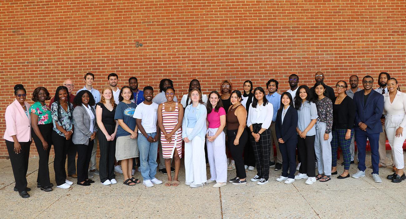 Group of people stand in front of a brick wall outside the School of Public Health.