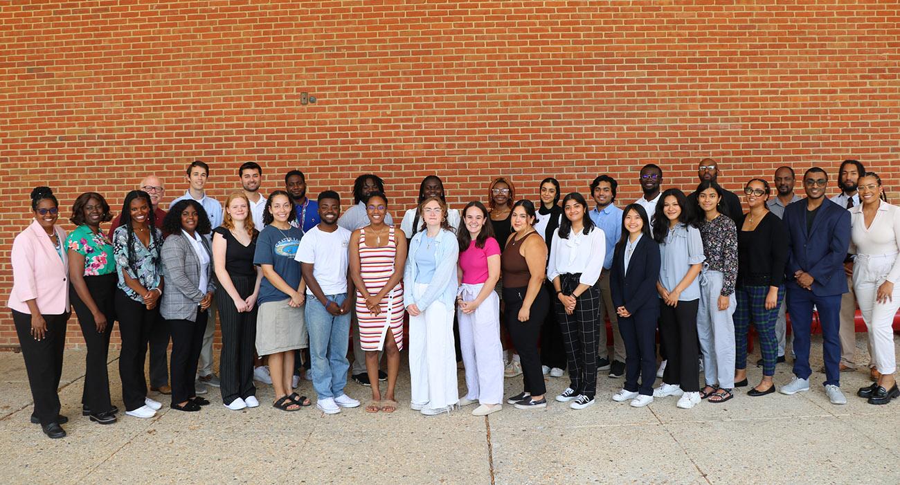 Group of people stand in front of a brick wall outside the School of Public Health.